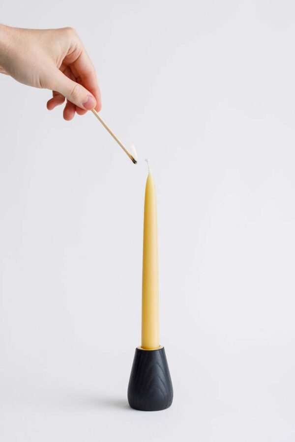 Image of small ebonised ash handmade wooden candle holder, with candle and hand showing it being lit